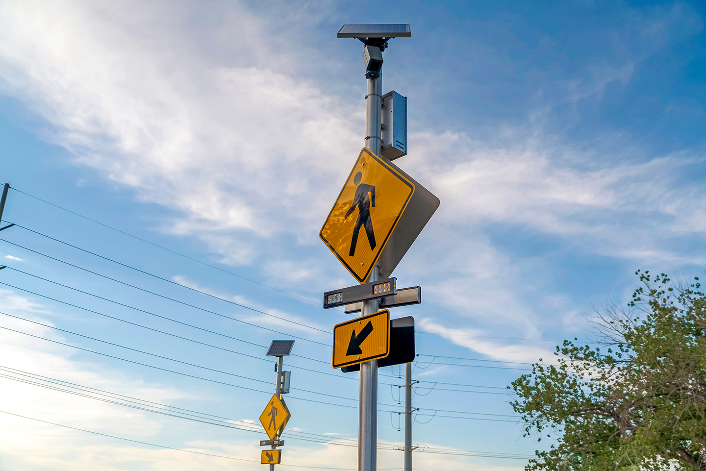 Yellow pedestrian crossing sign against a cloudy blue sky. Image Credit: AdobeStock_287869399