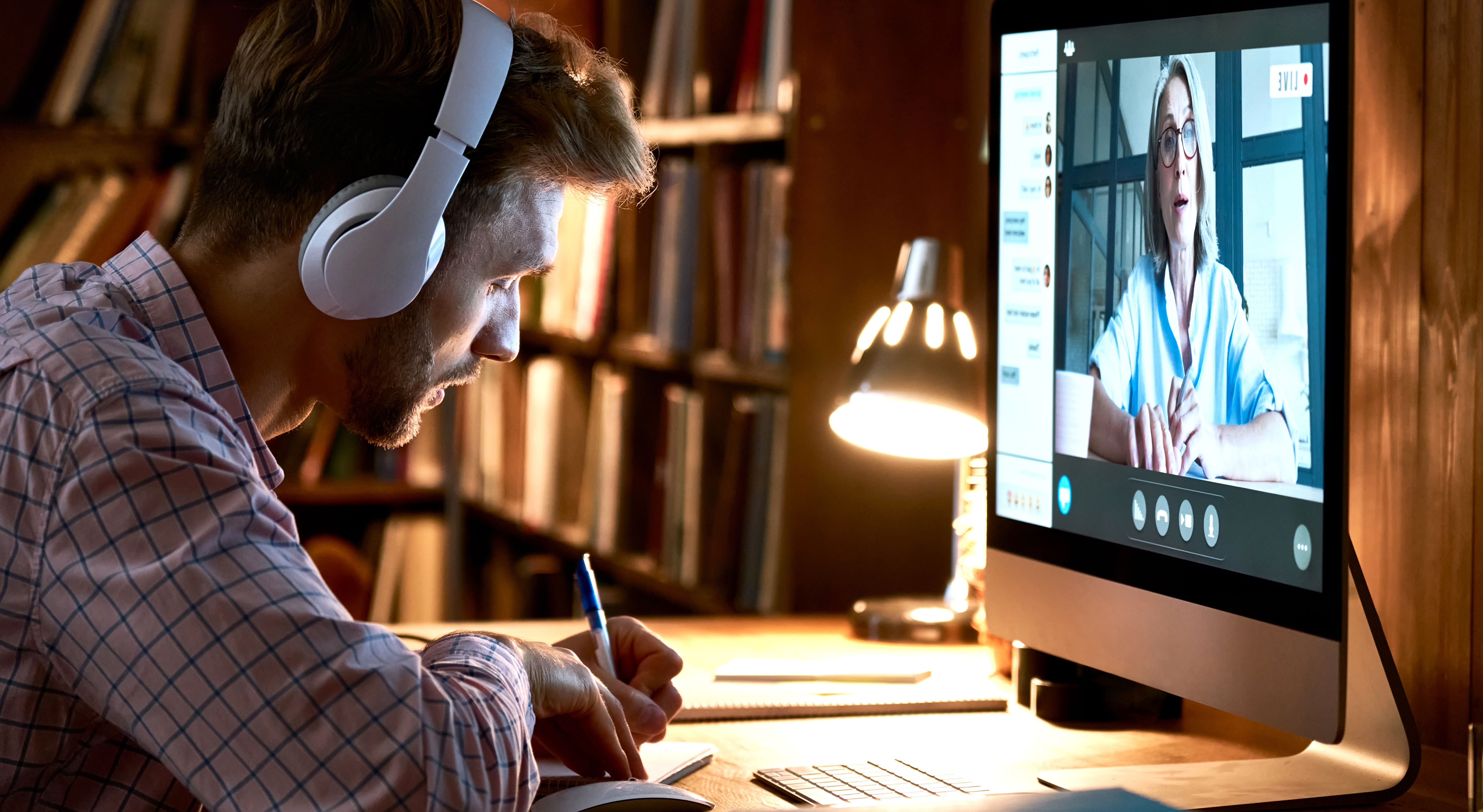 man wearing headphones is sitting at his desk in front of a computer. Image Credit: AdobeStock_392700319