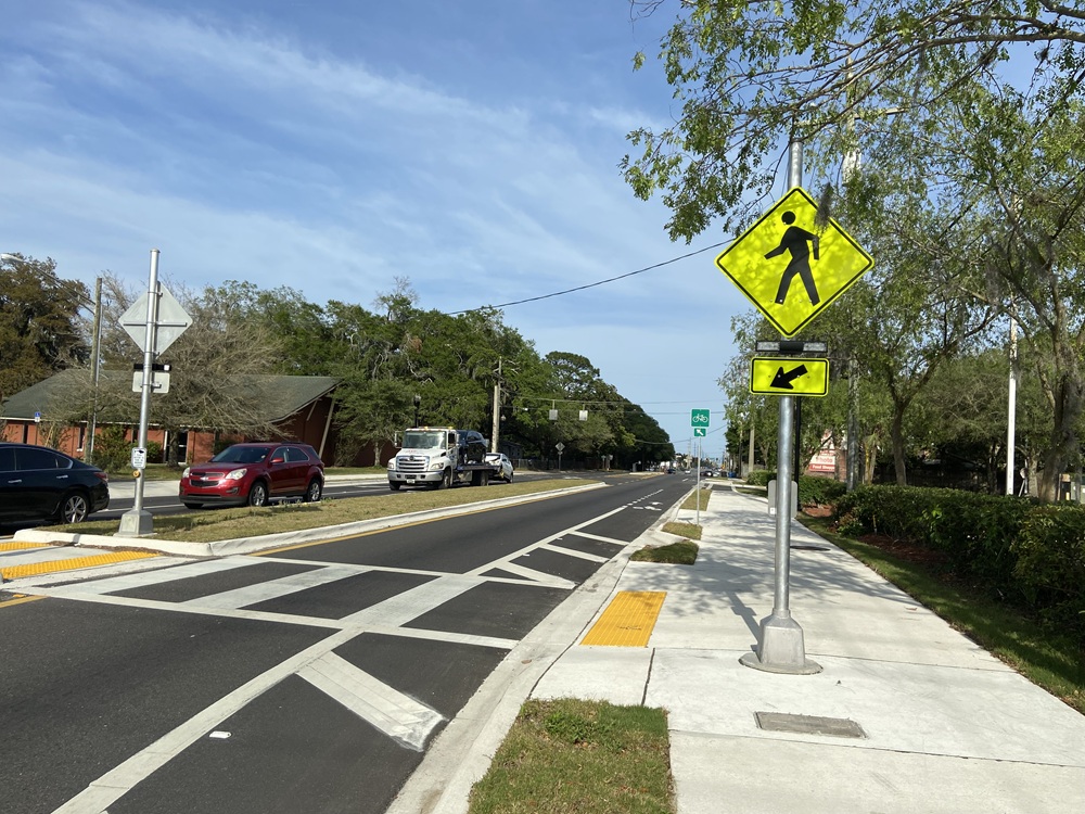 Road with cars stopped at a crosswalk with a yellow pedestrian crossing sign. Image Credit: FHWA